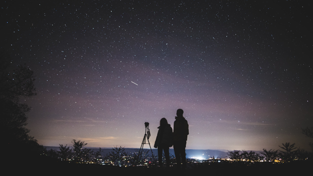 a couple of people standing on top of a hill under a night sky